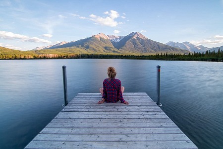 Zrelaksowana kobieta siedząca na pomoście, w tle widać jezioro i góry